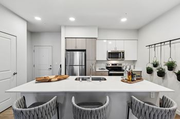 A modern kitchen with a white table and grey chairs.